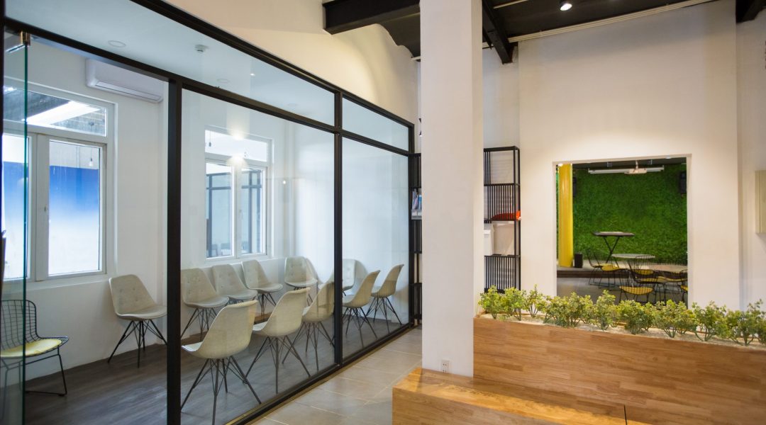 Nobody in office lobby with wooden bench. White wall with column and shelves. Green plants as part of interior. Many chairs behind glassy wall. Business center concept